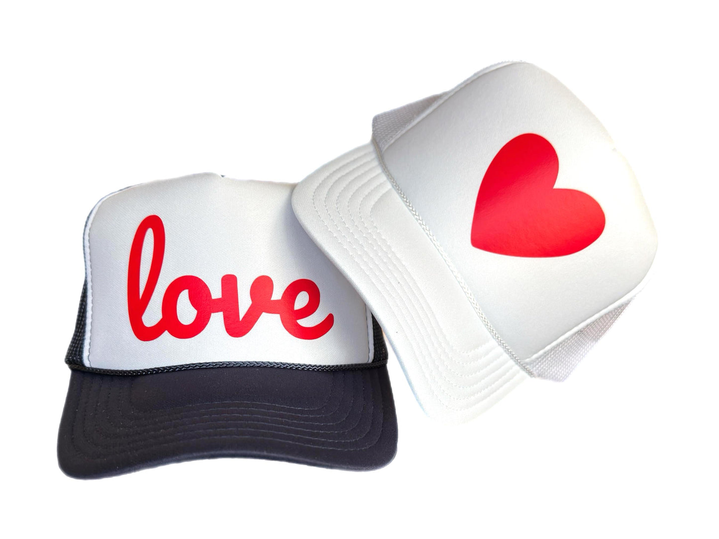 Trucker hat with word love in red script font on navy and white trucker hat, next to white trucker hat with a red heart.