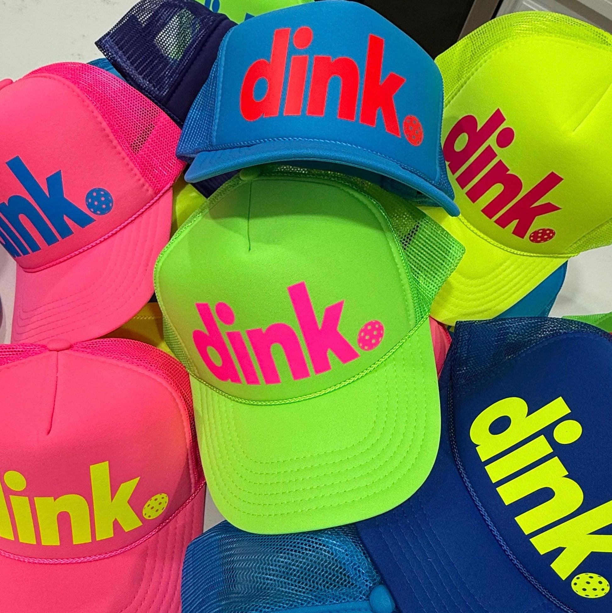 Assortment of colorful neon pickleball trucker hats with logo dink and a pickleball by stevi