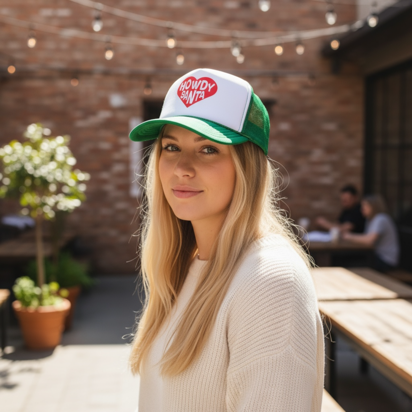 Woman wearing a green and white Otto snapback Christmas trucker hat with frestive red heart and  'Howdy Santa' words to elevate your holiday shopping attire. Great gift for holiday party or yourself!